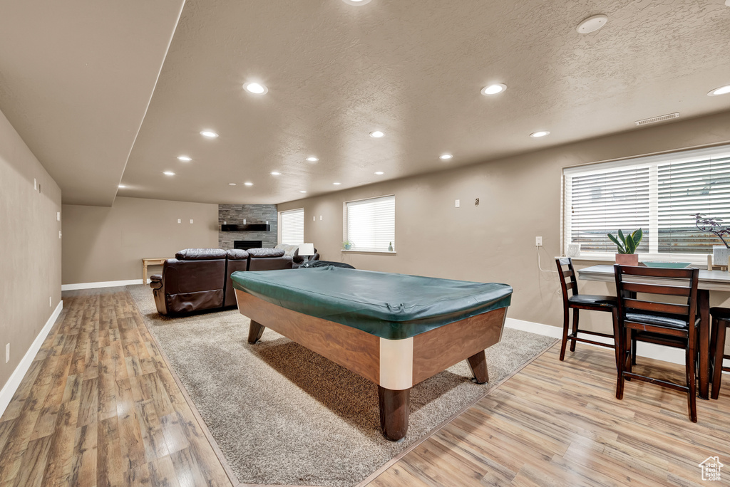 Recreation room with billiards, light hardwood / wood-style flooring, a textured ceiling, and a fireplace