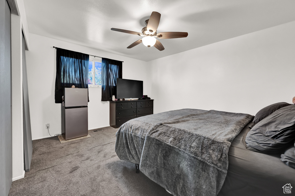 Bedroom with ceiling fan, light carpet, and stainless steel fridge