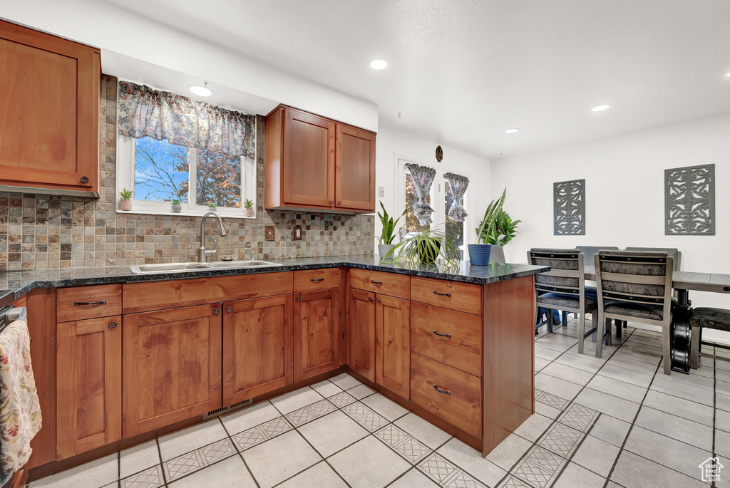 Kitchen with dark stone countertops, sink, backsplash, and light tile flooring