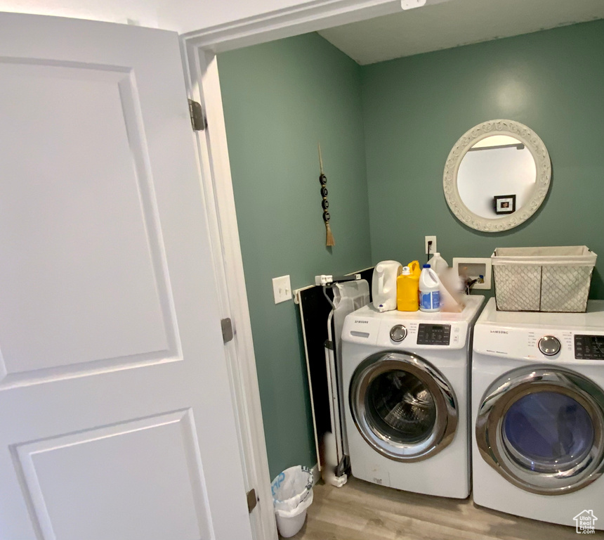 Clothes washing area with light hardwood / wood-style flooring, washing machine and clothes dryer, and washer hookup