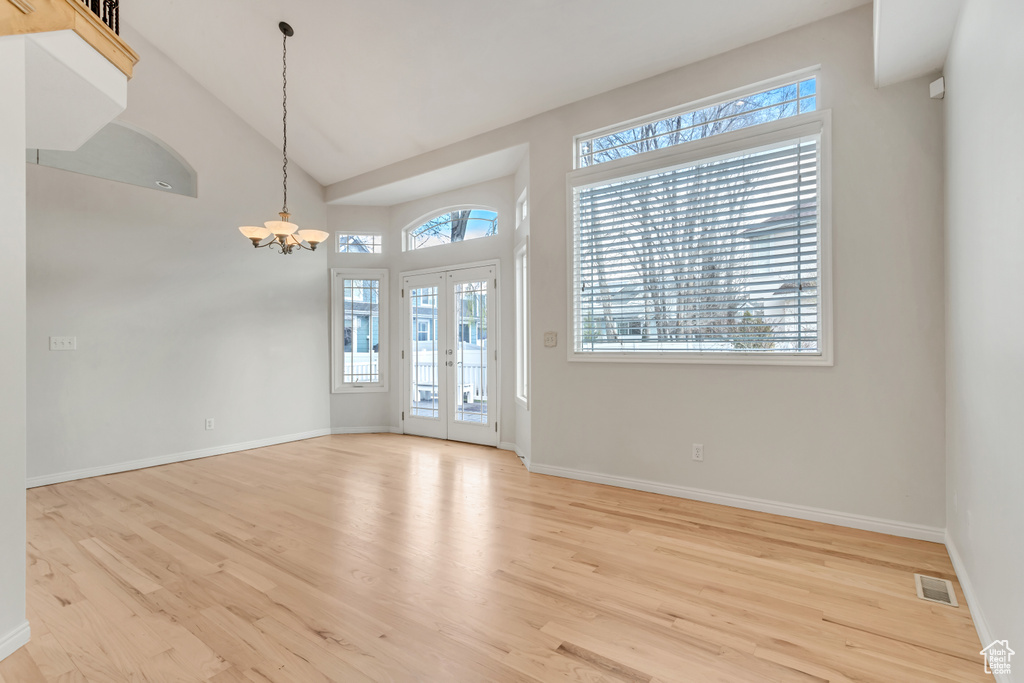 Unfurnished room featuring a notable chandelier, french doors, light wood-type flooring, and high vaulted ceiling