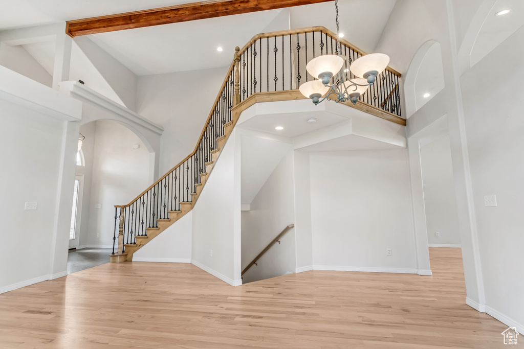 Stairs with high vaulted ceiling, light wood-type flooring, beam ceiling, and a chandelier