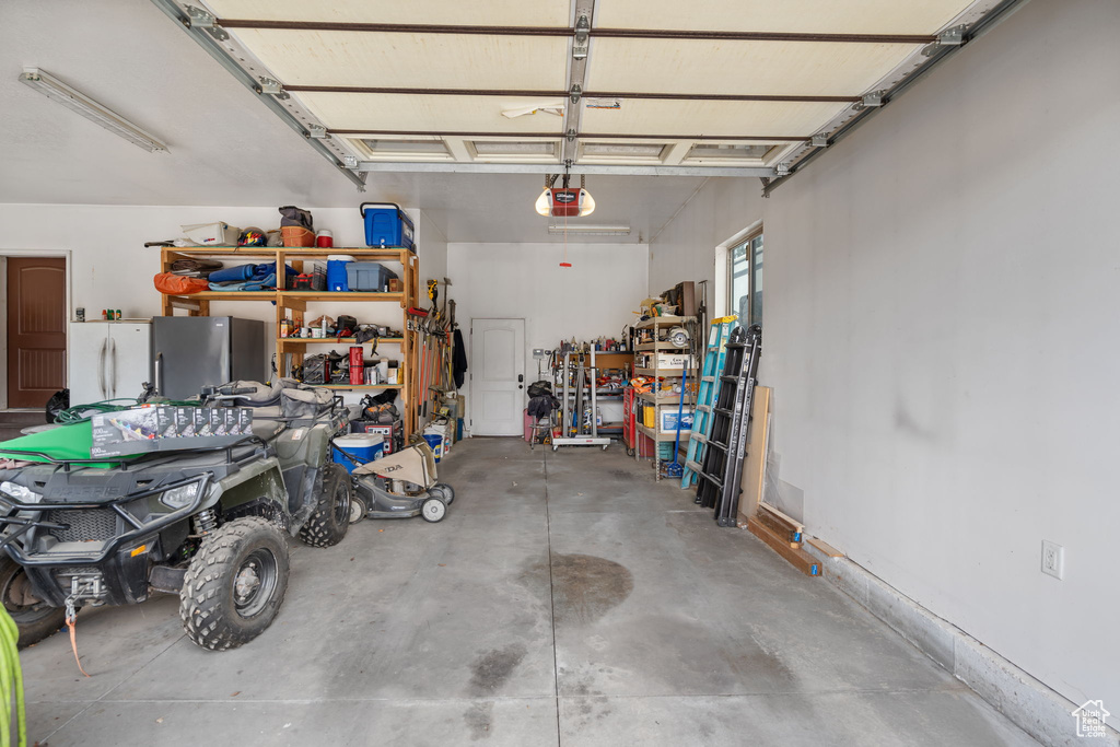 Garage featuring a garage door opener, white refrigerator, and stainless steel refrigerator