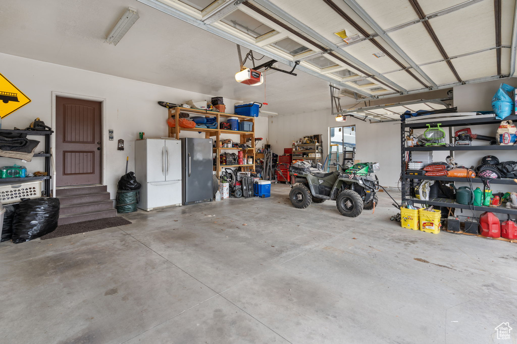 Garage featuring stainless steel refrigerator, a garage door opener, and white refrigerator