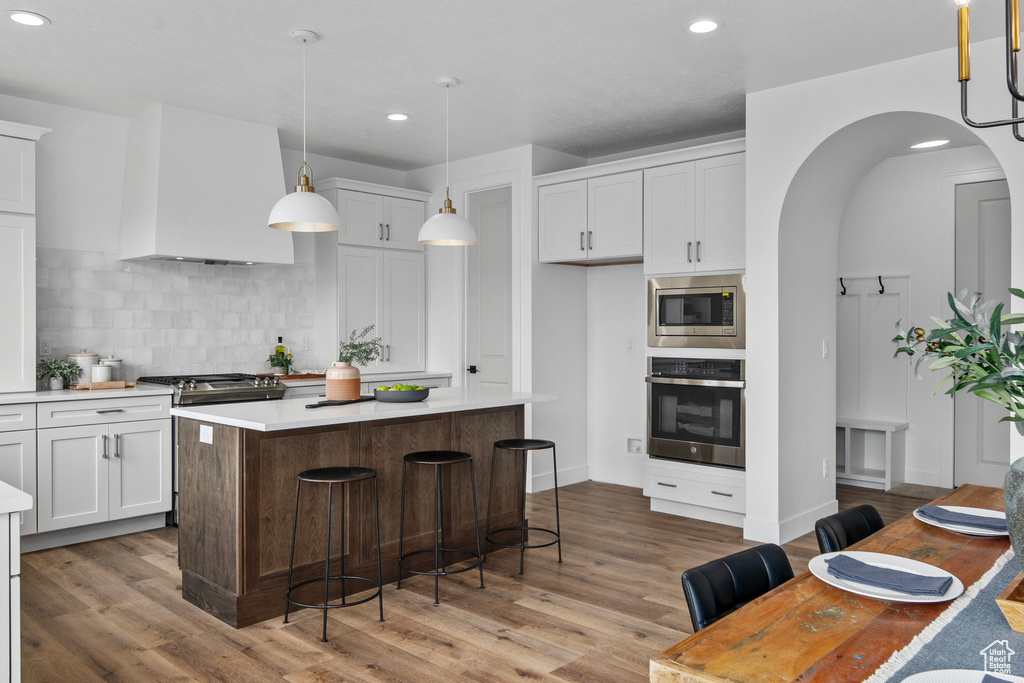 Kitchen featuring wood-type flooring, a center island, pendant lighting, tasteful backsplash, and appliances with stainless steel finishes