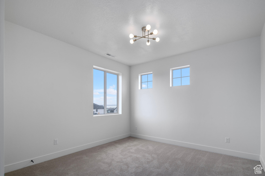 Unfurnished room with light colored carpet and a notable chandelier