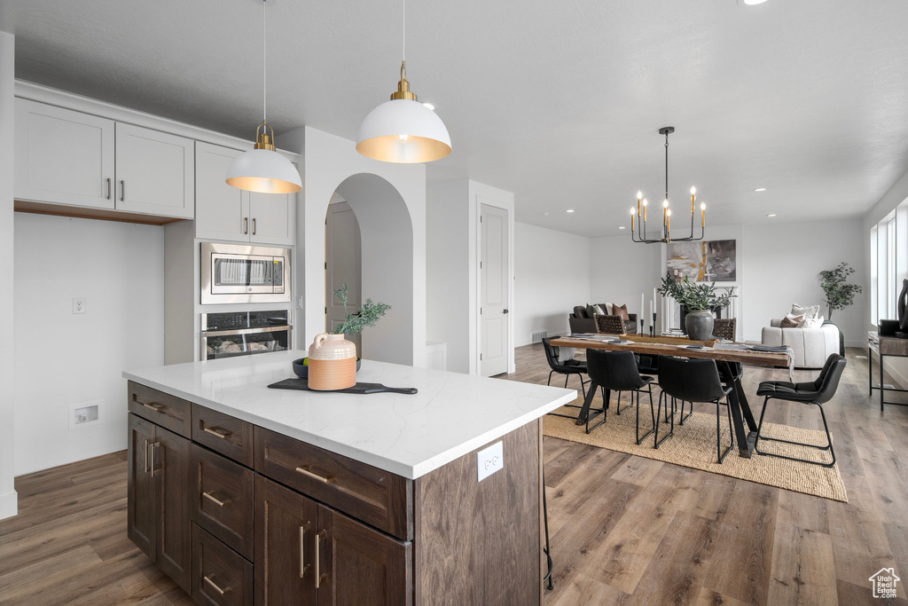 Kitchen featuring a notable chandelier, hardwood / wood-style flooring, hanging light fixtures, a kitchen island, and appliances with stainless steel finishes