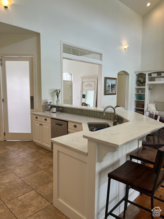 Kitchen featuring white cabinets, a breakfast bar area, sink, light stone countertops, and stainless steel dishwasher