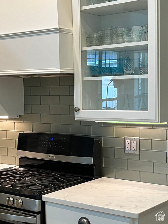Kitchen featuring stainless steel gas range, light stone countertops, and backsplash