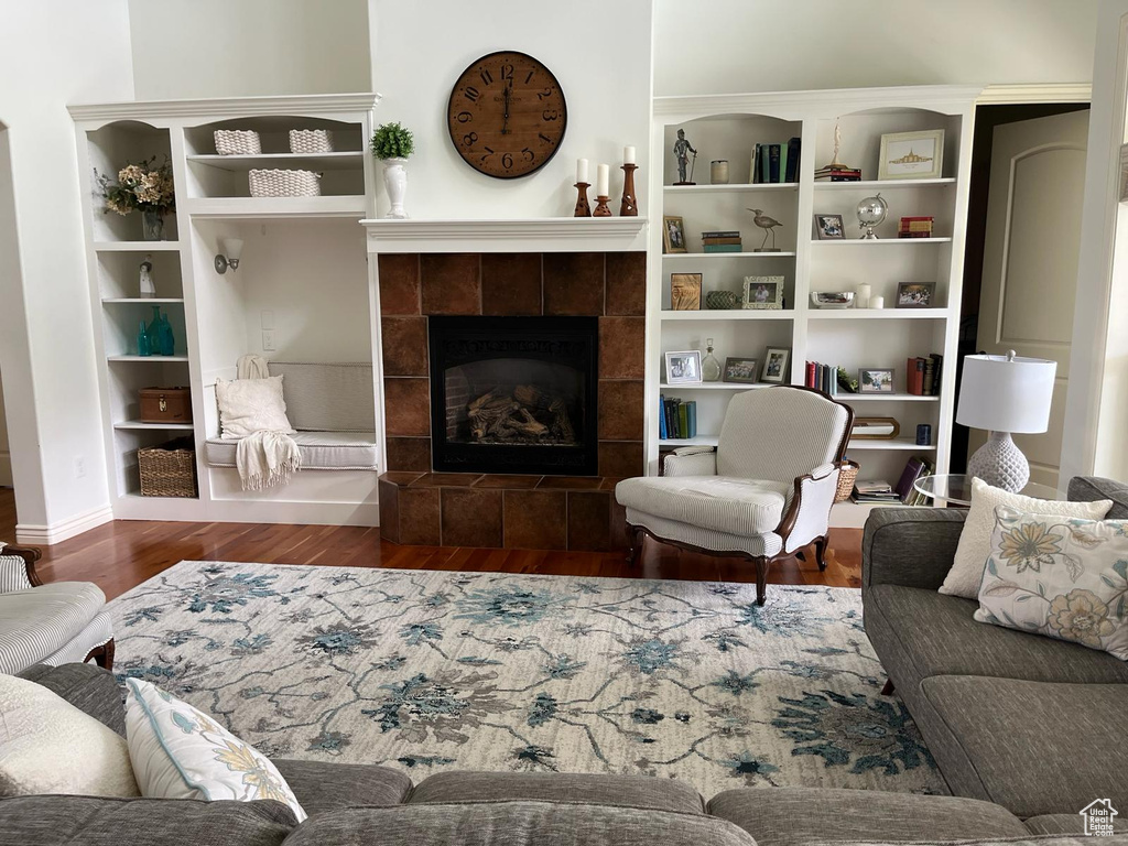 Living room featuring a tile fireplace, built in shelves, and dark wood-type flooring