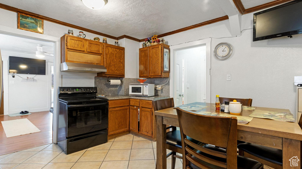Kitchen with ornamental molding, black electric range oven, a textured ceiling, tasteful backsplash, and light tile floors