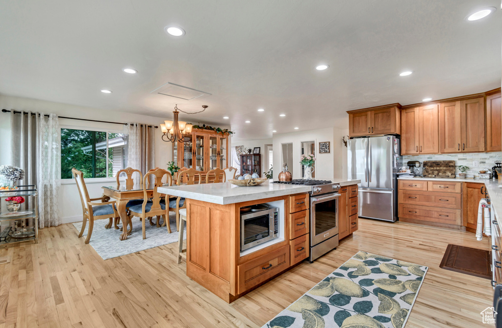 Kitchen featuring hanging light fixtures, appliances with stainless steel finishes, a chandelier, light hardwood / wood-style floors, and a center island