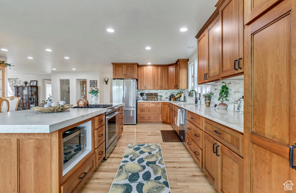 Kitchen with light hardwood / wood-style floors, a kitchen island, tasteful backsplash, appliances with stainless steel finishes, and sink