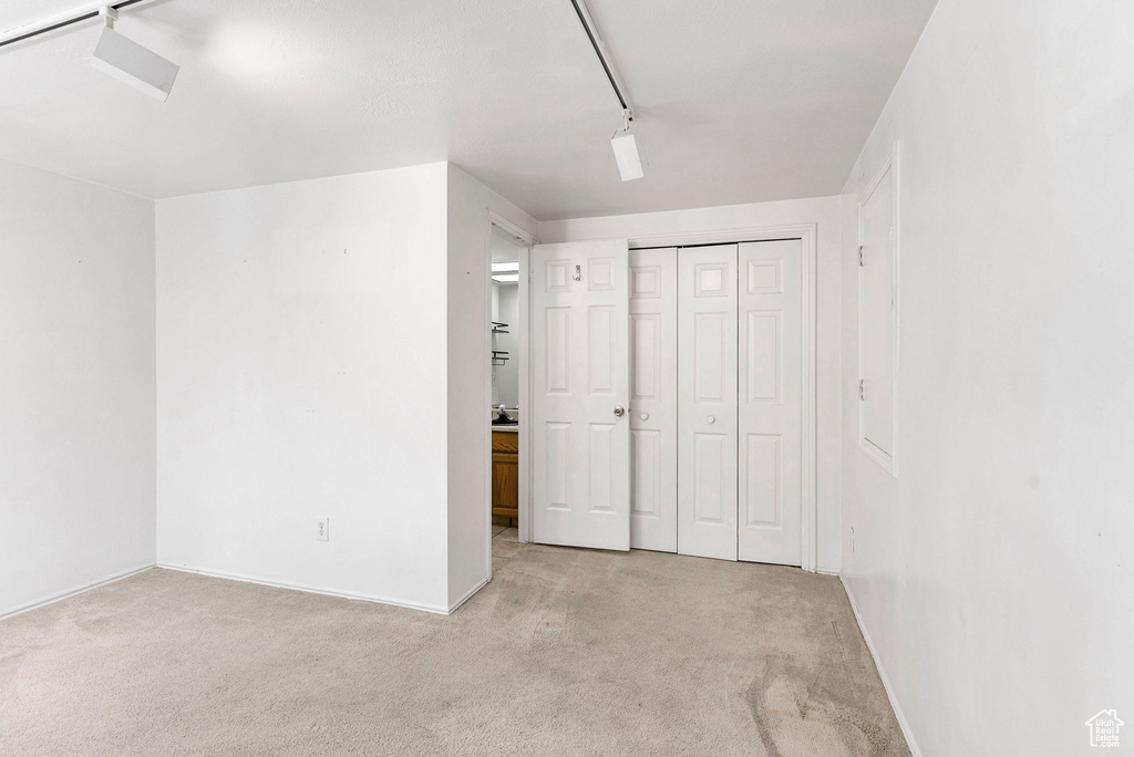 Unfurnished bedroom with a closet, light colored carpet, and track lighting