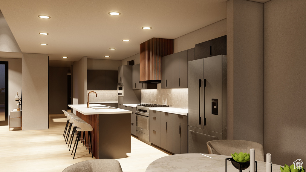 Kitchen with light hardwood / wood-style floors, high end refrigerator, an island with sink, tasteful backsplash, and a breakfast bar