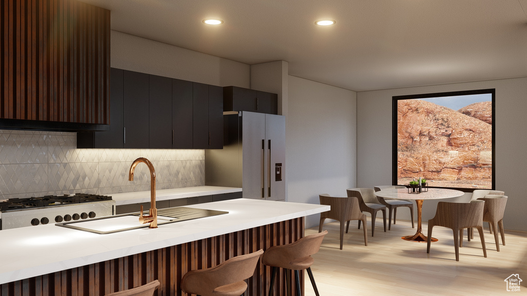 Kitchen featuring a breakfast bar, sink, light wood-type flooring, tasteful backsplash, and wall chimney range hood