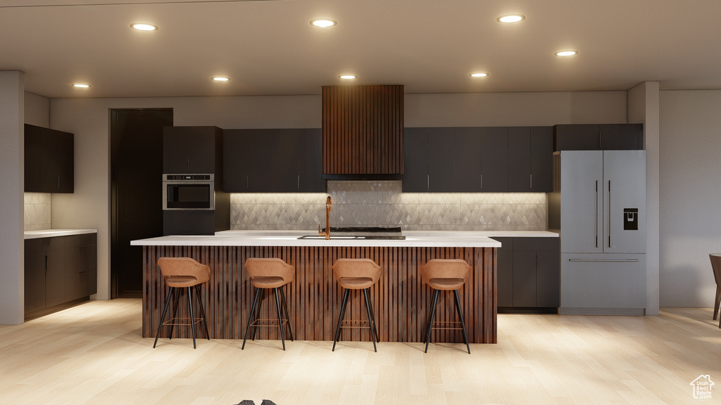 Kitchen with tasteful backsplash, fridge, light hardwood / wood-style floors, and a center island with sink