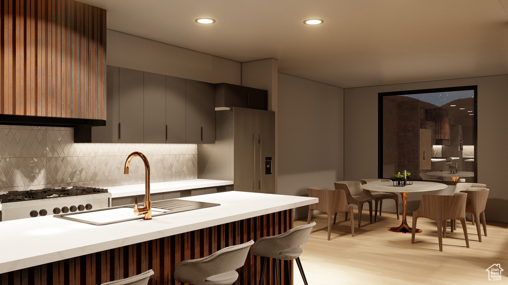 Kitchen featuring a breakfast bar, sink, light hardwood / wood-style flooring, range, and tasteful backsplash