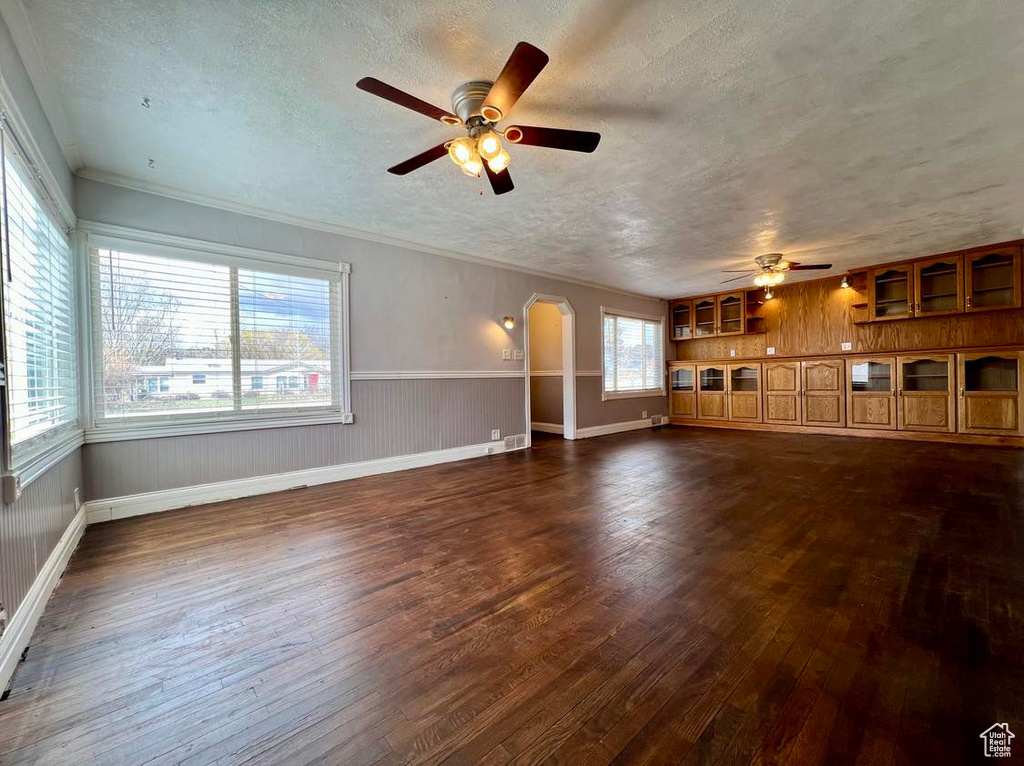 Unfurnished living room featuring crown molding, dark hardwood / wood-style floors, a textured ceiling, and ceiling fan