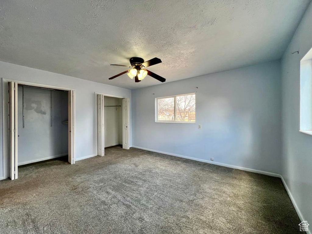 Unfurnished bedroom with two closets, a textured ceiling, ceiling fan, and dark carpet