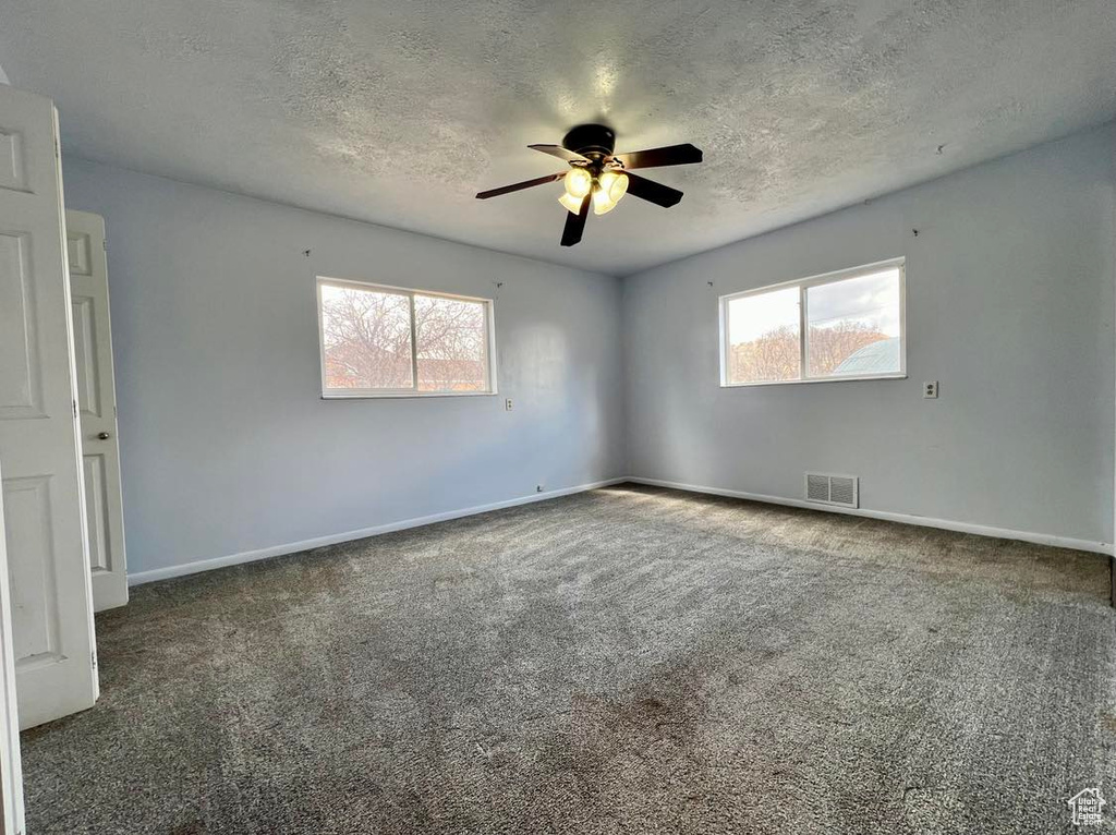 Empty room with ceiling fan, dark carpet, and a wealth of natural light