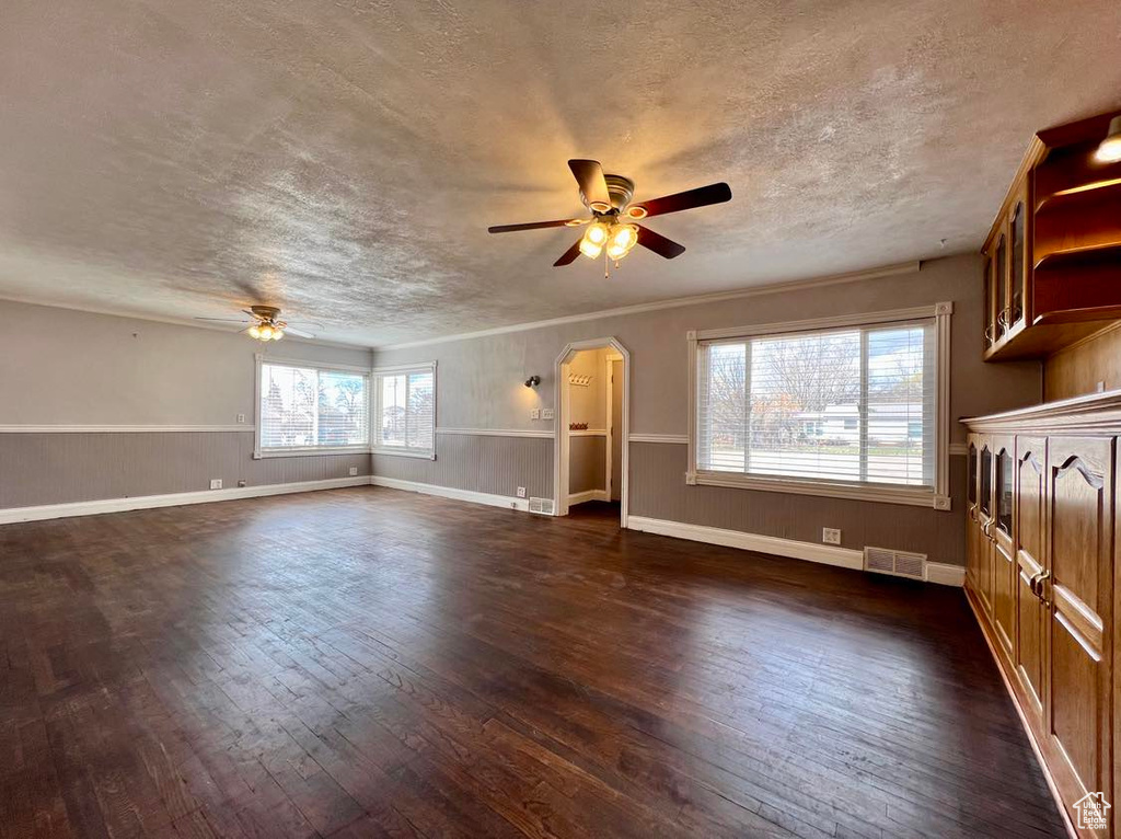 Unfurnished living room featuring a healthy amount of sunlight, ceiling fan, and dark wood-type flooring
