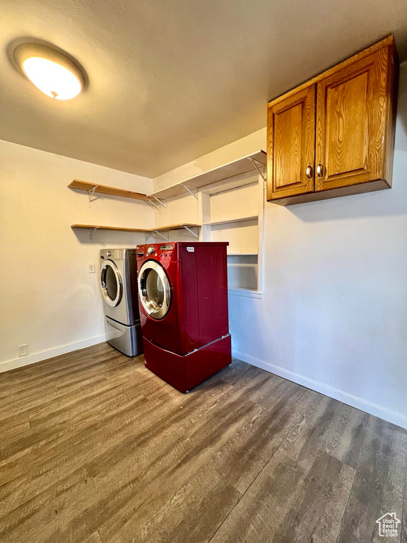Washroom with dark hardwood / wood-style floors, cabinets, and washing machine and dryer
