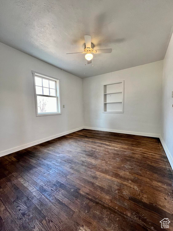 Empty room with built in features, a textured ceiling, ceiling fan, and dark hardwood / wood-style floors