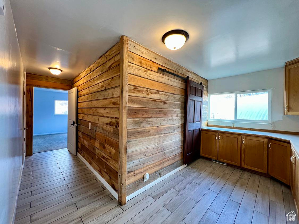 Corridor with a barn door, a healthy amount of sunlight, wood walls, and light wood-type flooring
