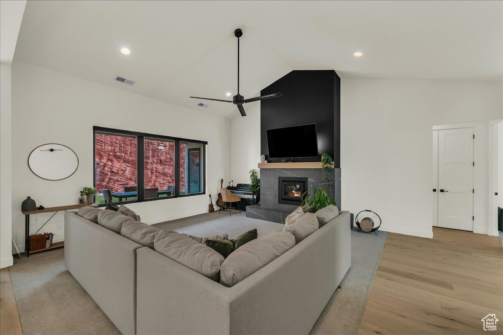 Living room with a tile fireplace, ceiling fan, light hardwood / wood-style flooring, and high vaulted ceiling