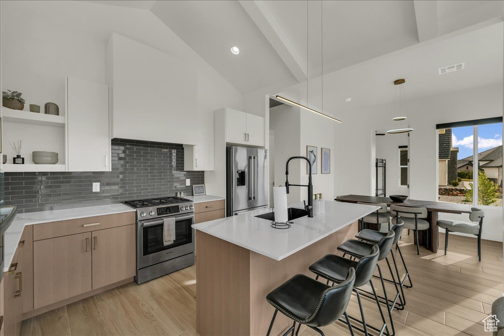 Kitchen featuring high end appliances, decorative light fixtures, a kitchen island with sink, and light wood-type flooring