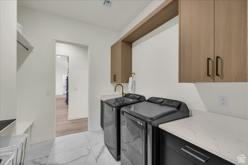 Washroom featuring washer and dryer, light tile floors, and cabinets