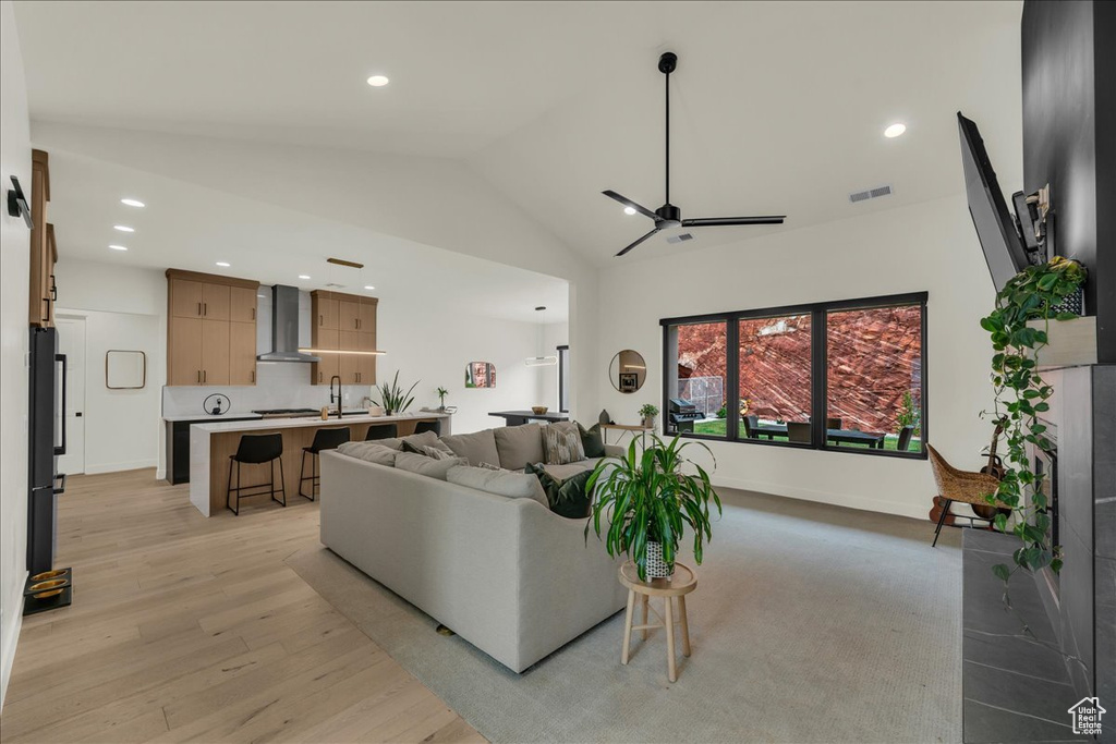 Living room featuring high vaulted ceiling, ceiling fan, light wood-type flooring, and sink