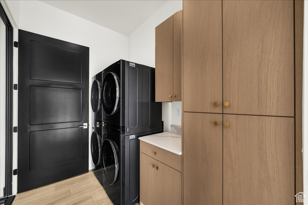 Laundry area with stacked washer and clothes dryer, cabinets, and light hardwood / wood-style flooring