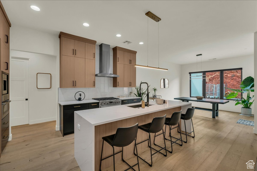 Kitchen with wall chimney exhaust hood, a center island with sink, high end stainless steel range, and pendant lighting