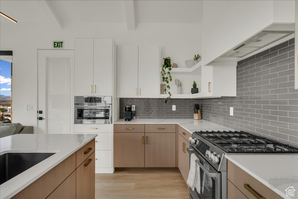 Kitchen with white cabinetry, backsplash, beamed ceiling, light wood-type flooring, and stainless steel appliances