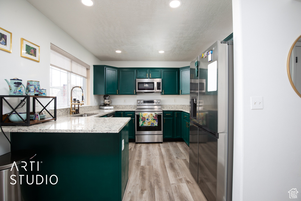 Kitchen with stainless steel appliances, sink, light stone countertops, kitchen peninsula, and light hardwood / wood-style floors