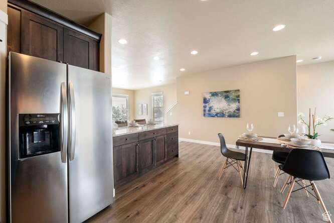 Kitchen featuring dark wood-type flooring, light stone counters, stainless steel refrigerator with ice dispenser, and dark brown cabinetry