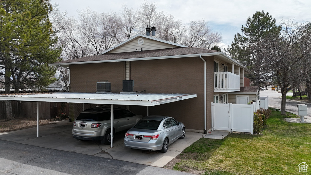 View of side of property featuring a lawn, a balcony, a carport, and central AC unit