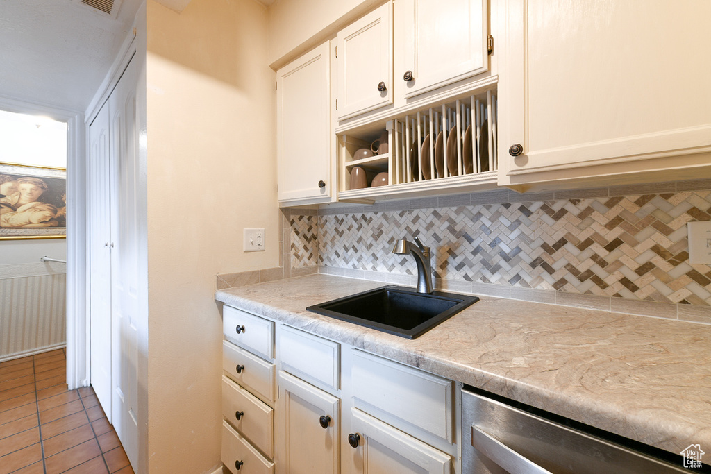 Kitchen featuring tasteful backsplash, sink, dark tile flooring, white cabinets, and light stone counters
