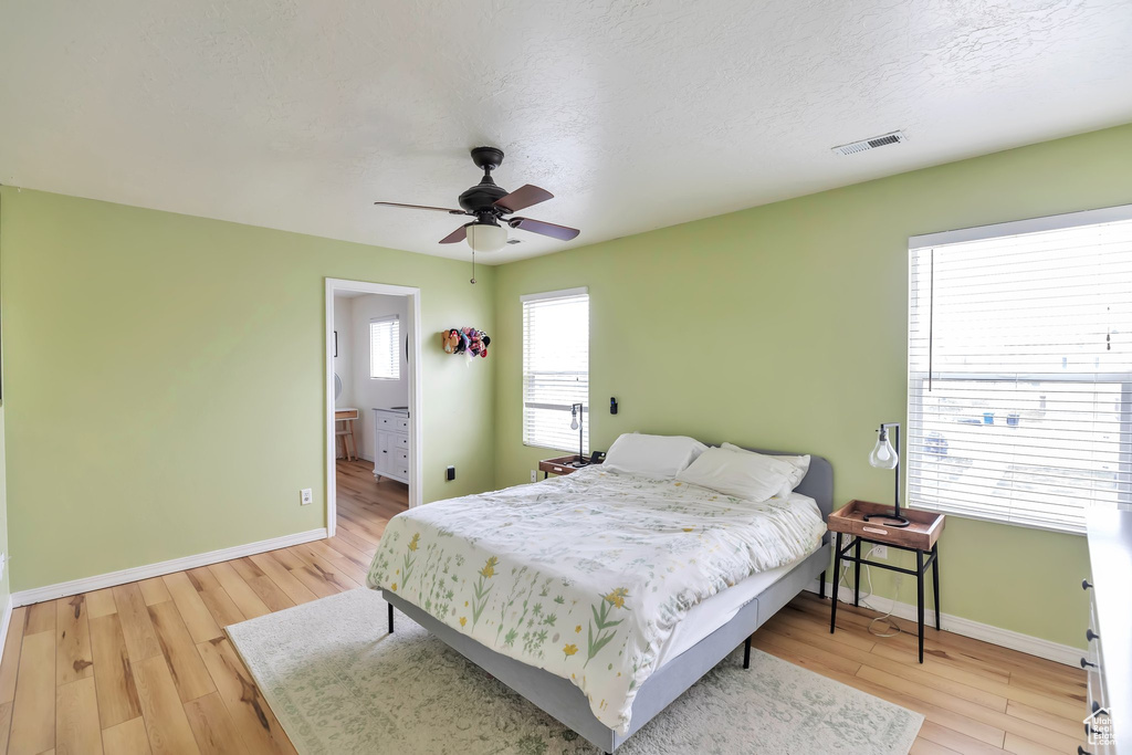 Bedroom with multiple windows, ensuite bath, light wood-type flooring, and ceiling fan