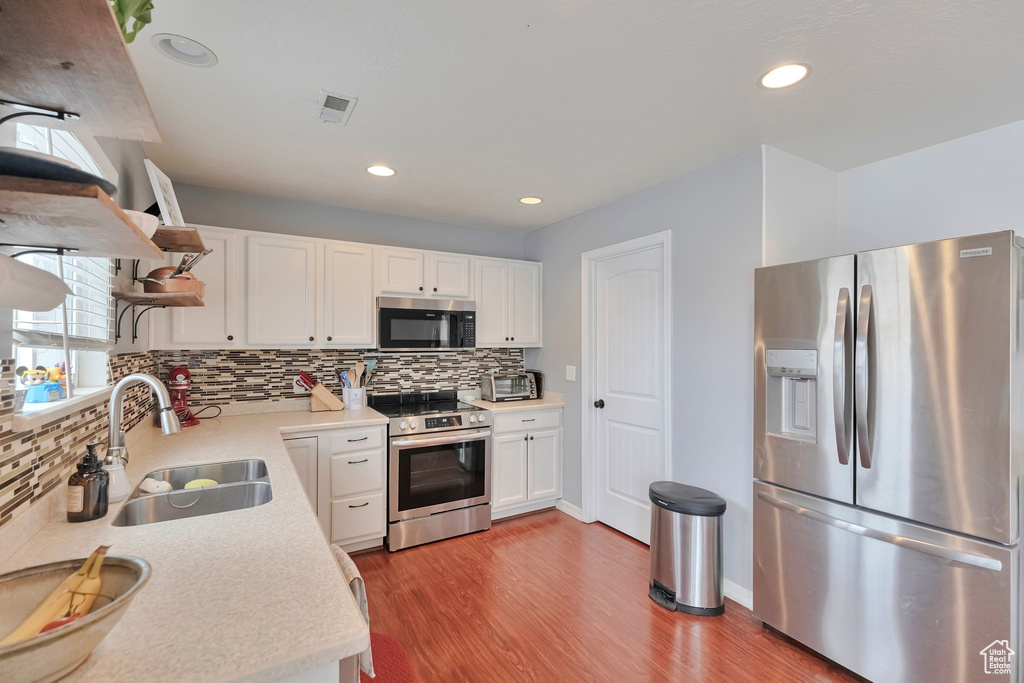 Kitchen featuring hardwood / wood-style flooring, white cabinetry, appliances with stainless steel finishes, backsplash, and sink
