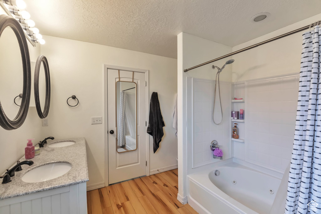Bathroom with vanity with extensive cabinet space, a textured ceiling, double sink, shower / bath combo, and wood-type flooring