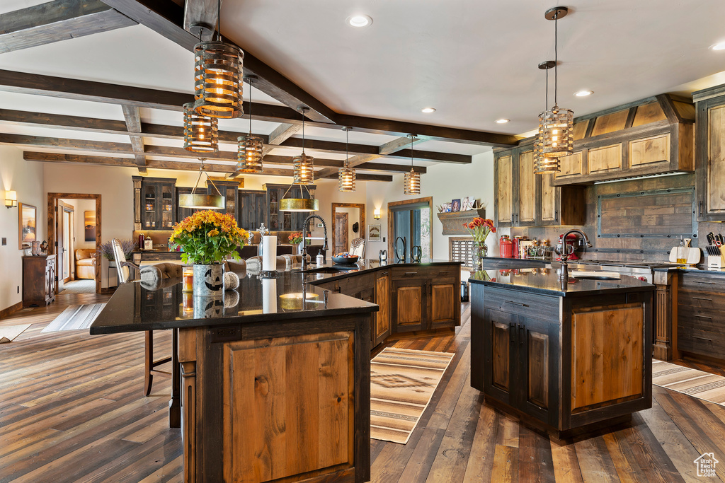 Kitchen with pendant lighting, a large island with sink, beamed ceiling, backsplash, and a kitchen bar
