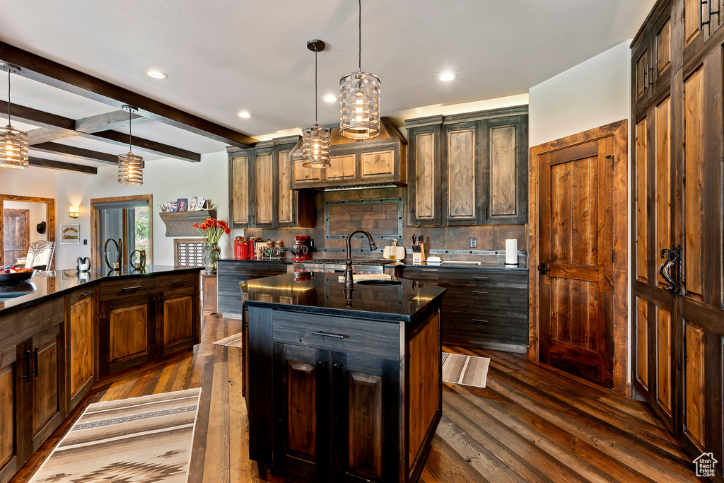 Kitchen featuring backsplash, a kitchen island with sink, pendant lighting, and dark wood-type flooring