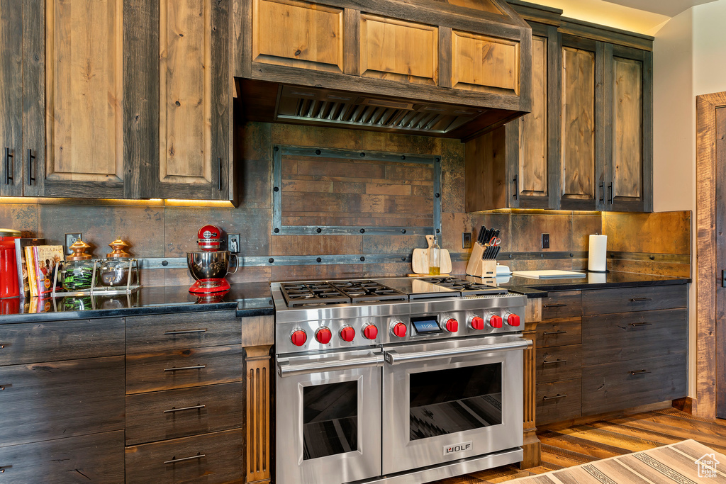 Kitchen featuring range with two ovens, backsplash, hardwood / wood-style floors, and dark brown cabinets