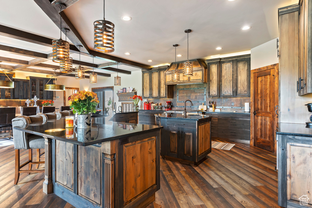Kitchen featuring a kitchen breakfast bar, a kitchen island with sink, dark hardwood / wood-style flooring, and beamed ceiling