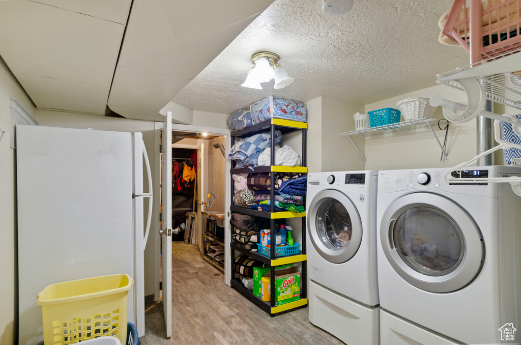 Laundry room featuring washing machine and clothes dryer, light hardwood / wood-style floors, and a textured ceiling