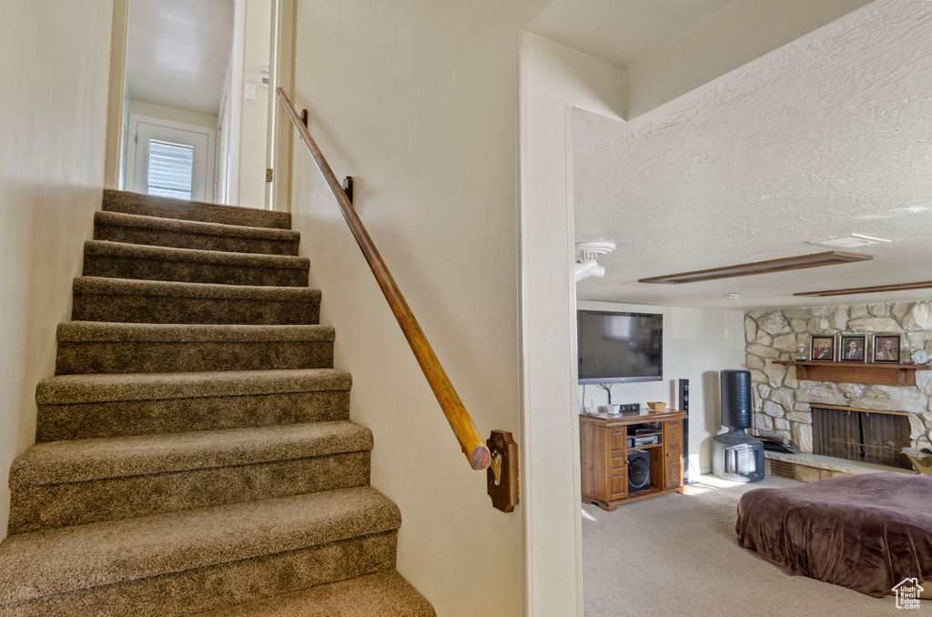Staircase featuring light carpet, a textured ceiling, and a fireplace