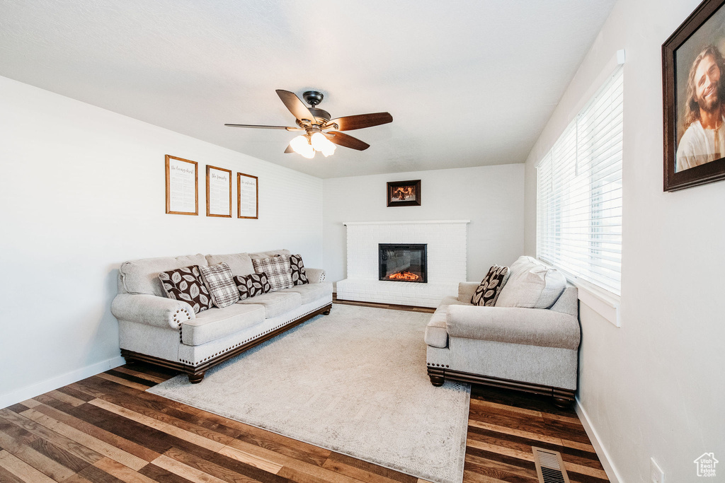 Living room featuring dark wood-type flooring, ceiling fan, and a fireplace